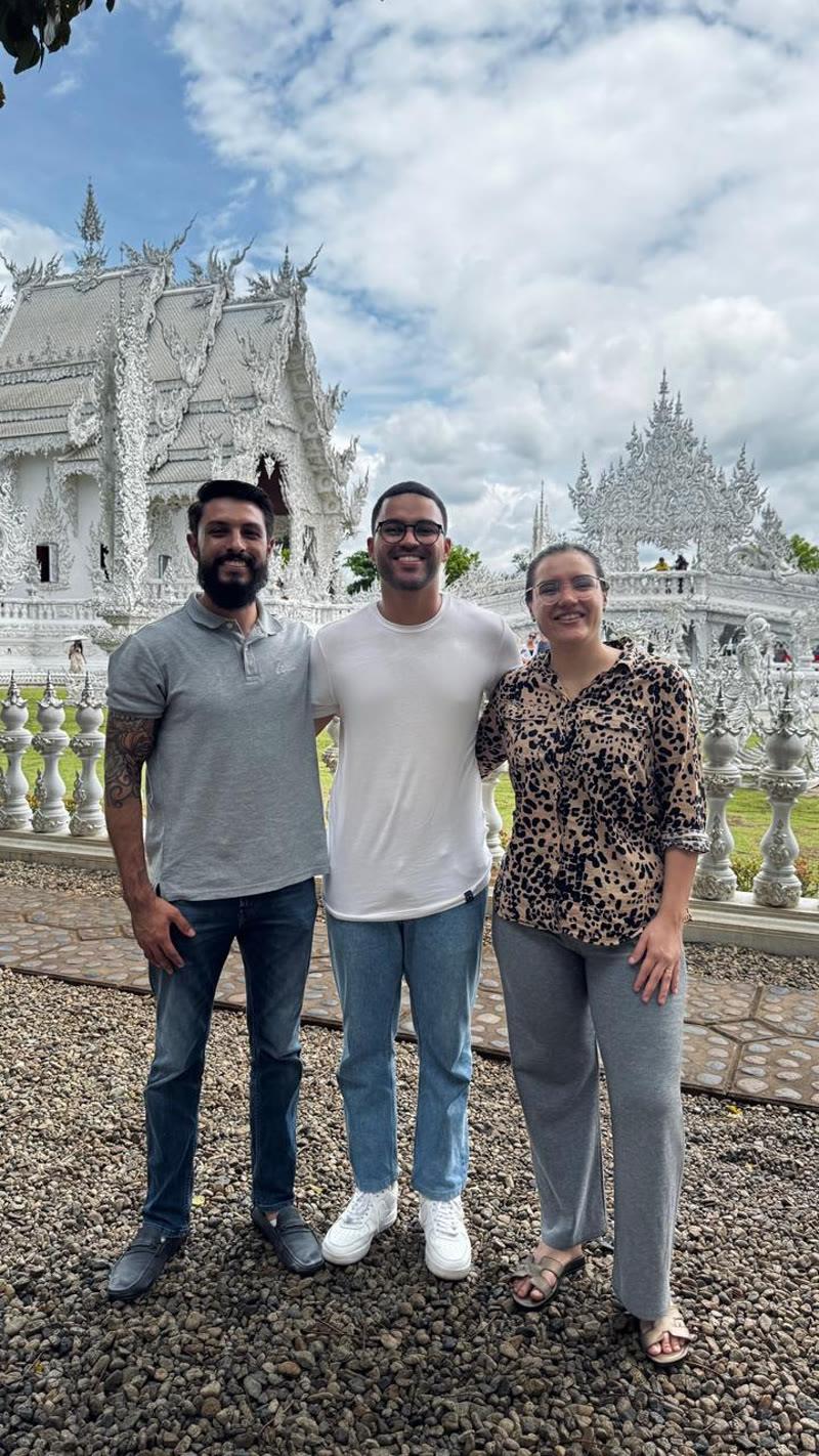 Guilherme, Aline e Gabriel diante de um templo branco, na Tailândia