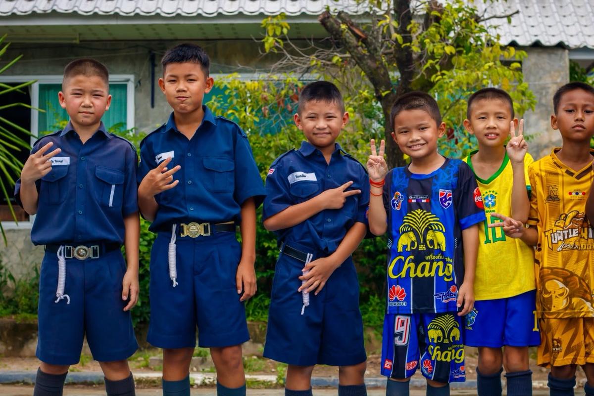 Crianças de uniforme e de camisa de futebol, sorrindo e fazendo sinais com as mãos